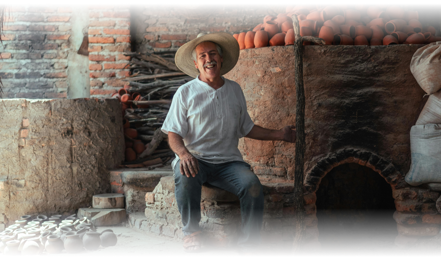 Older, Hispanic gentleman in front of a pottery kiln. He is smiling wide and appears very friendly.