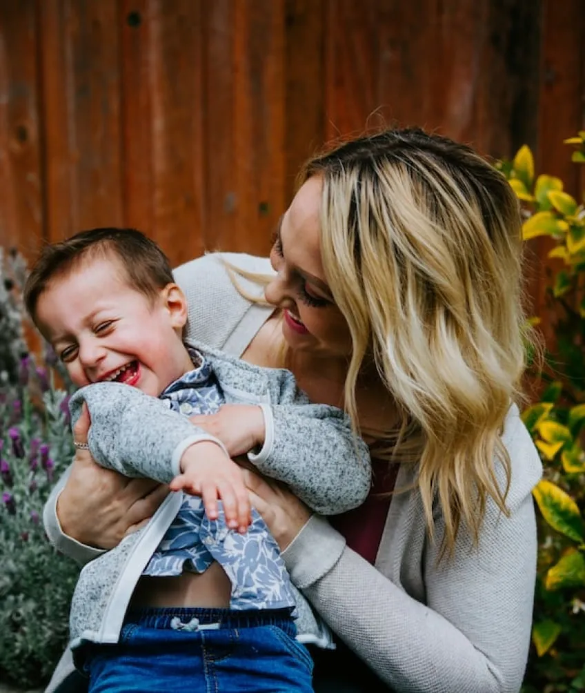 A woman smiling, holding a child who is laughing and smiling.