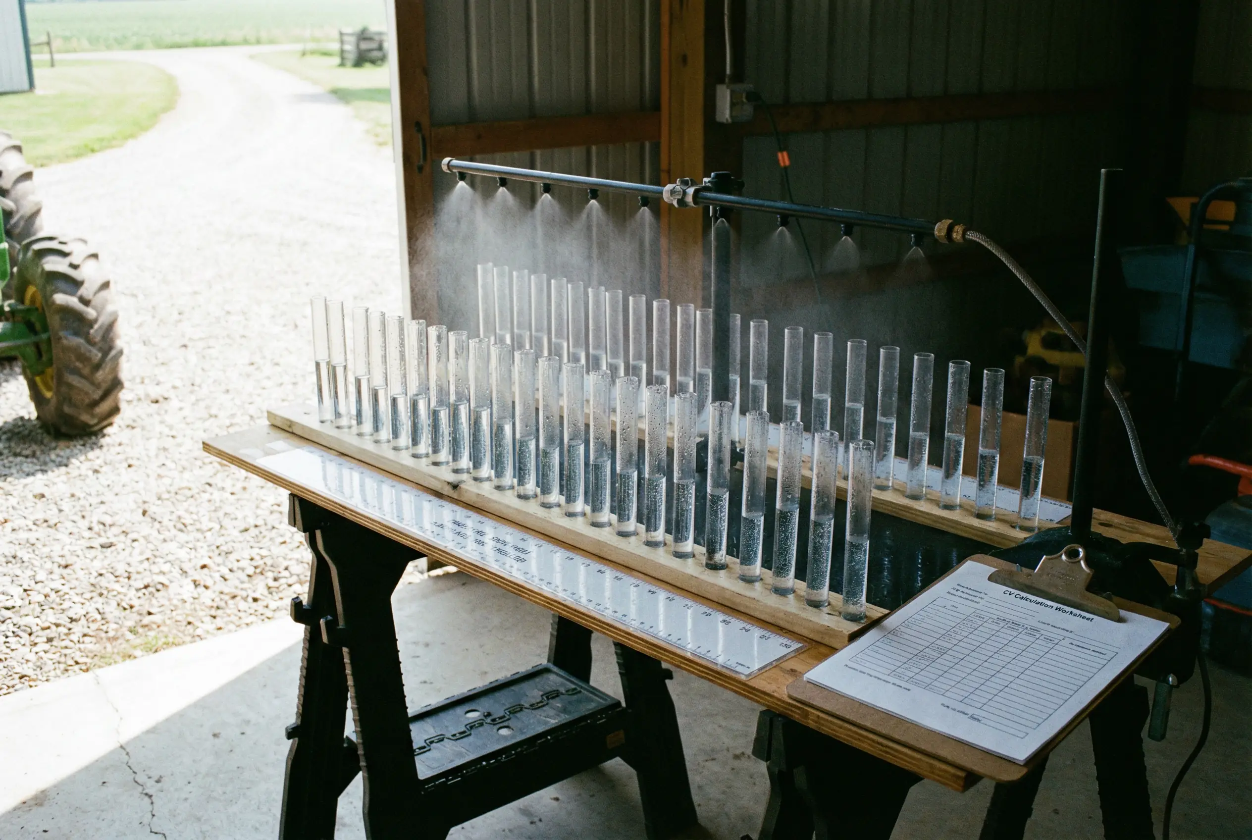 Spray pattern testing table with multiple clear collectors showing uneven fill levels used to check boom uniformity.