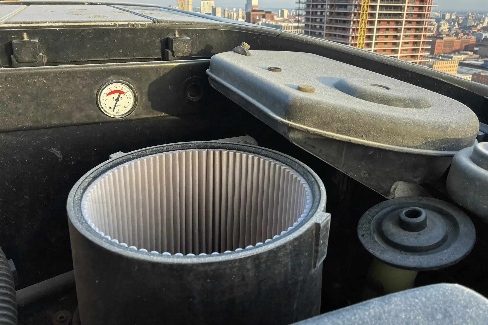 Komatsu excavator engine air cleaner housing with clogged filter element and restriction indicator showing red zone on Manhattan construction site
