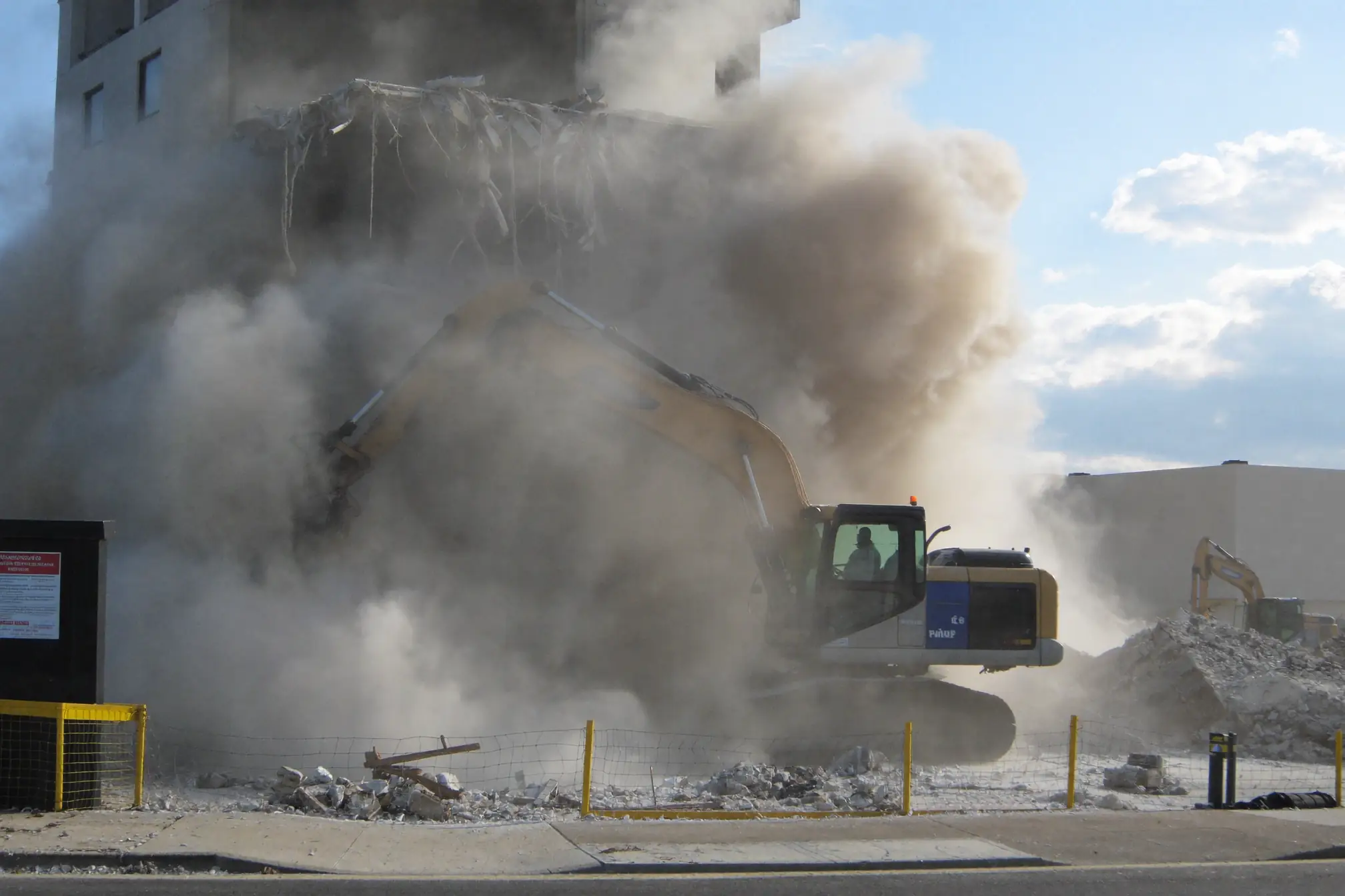 Volvo excavator with hydraulic breaker creating large demolition dust cloud during building demolition in South Bronx NYC construction site