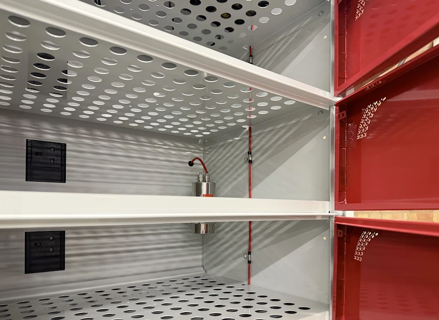 Interior of a metal cabinet with perforated shelves, red wiring, and electrical outlets on the side.