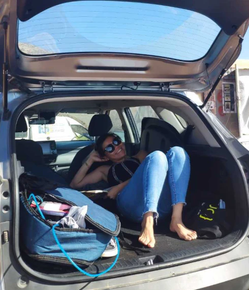 A Konpo team member relaxing barefoot in the open boot of a car on a sunny day