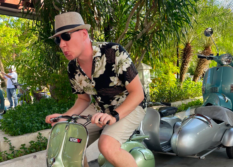 A Konpo team member in a straw hat and floral shirt hopping on a green Vespa