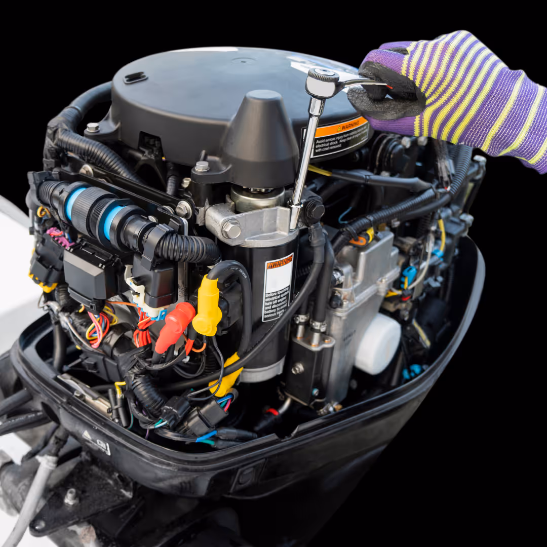 Gloved hand using a ratchet wrench on a black outboard boat motor with exposed wiring and engine components.