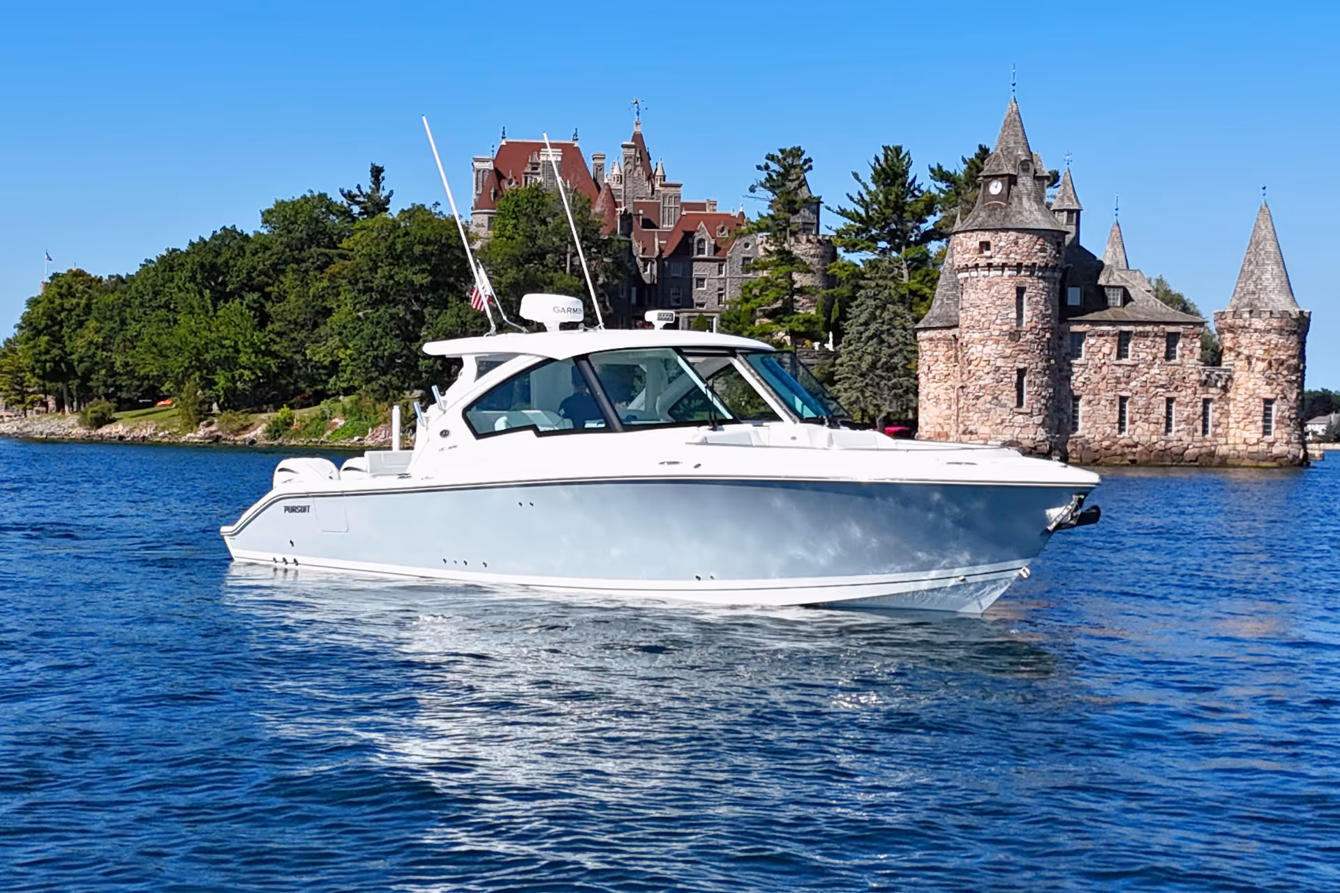 White luxury motorboat cruising on blue water with trees and stone castle in the background.