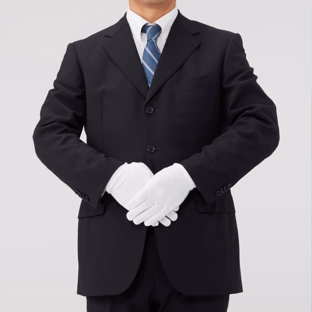 Person wearing a dark suit with a white shirt and blue striped tie, holding hands clasped in front while wearing white gloves.