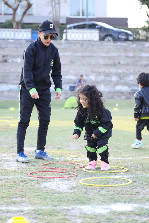 A young student jumps through hoops while her coach provides a helping hand