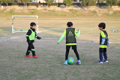 2 young students watch as a player in the middle is protecting the ball with her feet