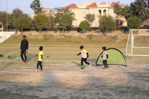 A young student dribbles with the ball, two other students chase him while a coach observes