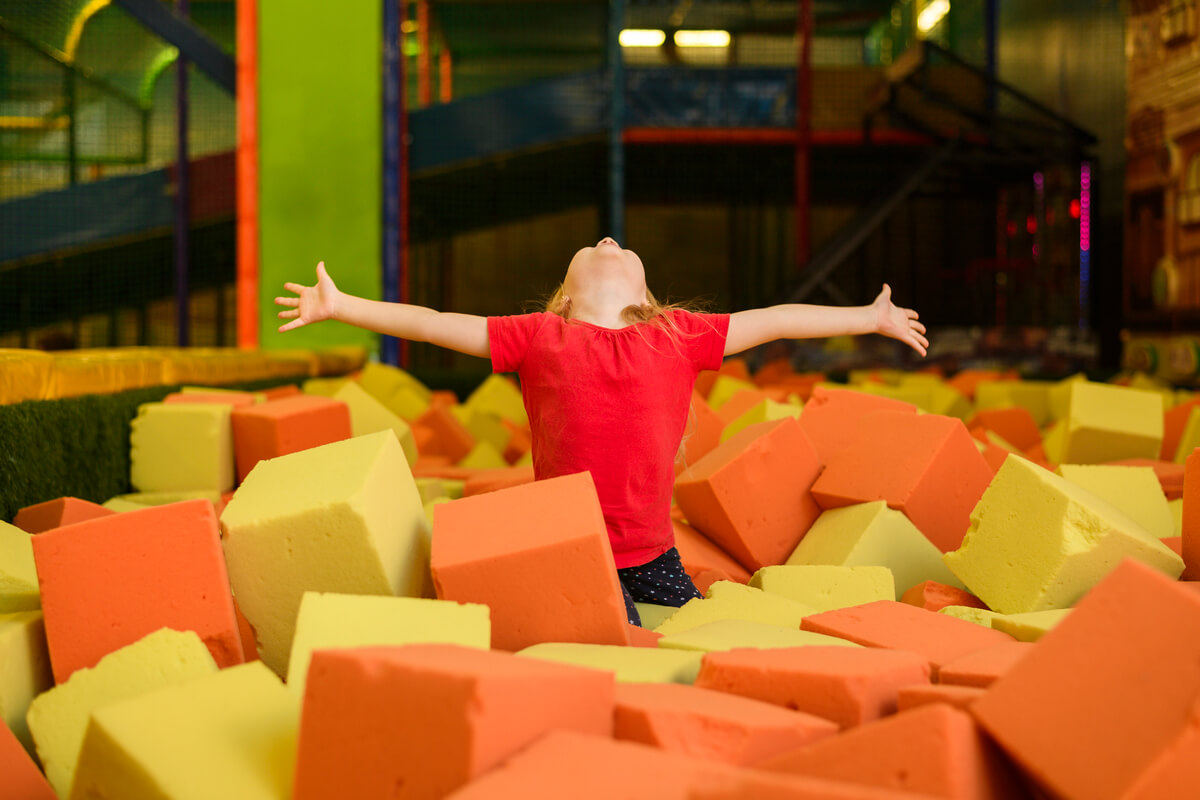 Barn med armene utstrakt står i et basseng fylt med fargerike skumklosser på en trampolinepark