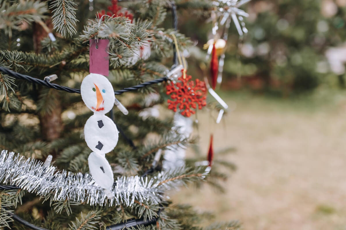 Hjemmelaget snømannpynt henger på et juletre dekorert med glitter og juleornamenter
