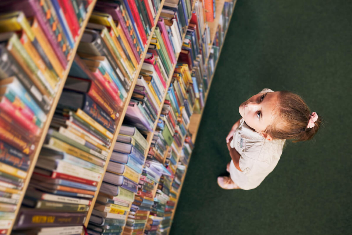 Lite barn ser opp på en bokhylle full av fargerike bøker på biblioteket
