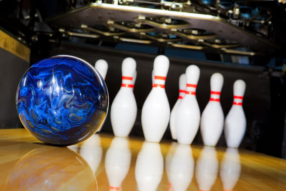 En blå bowlingkule ligger klar på banen foran en rad med hvite kjegler i et bowlinganlegg