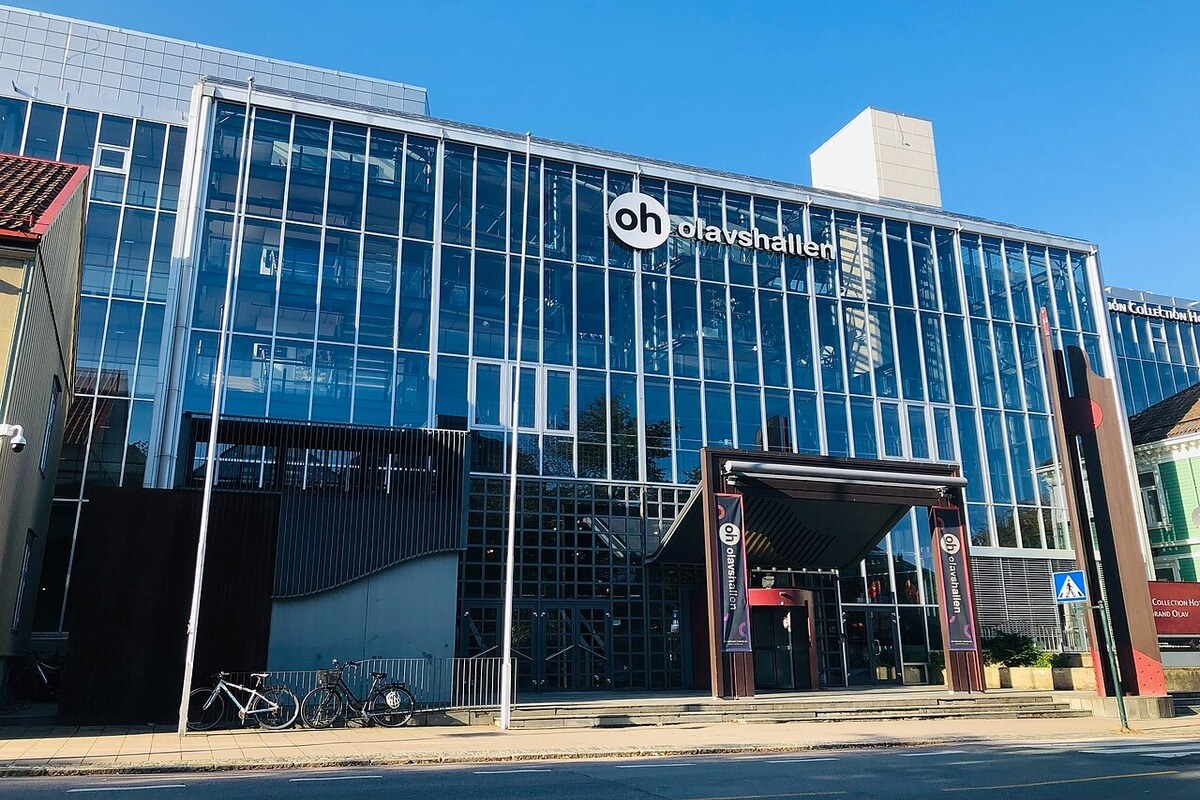 Fronten til Olavshallen i Trondheim, en glassvegg med overbygget inngangsparti og et skilt med logoen OH og Olasvhallen synlig øverst på veggen over inngangspartiet