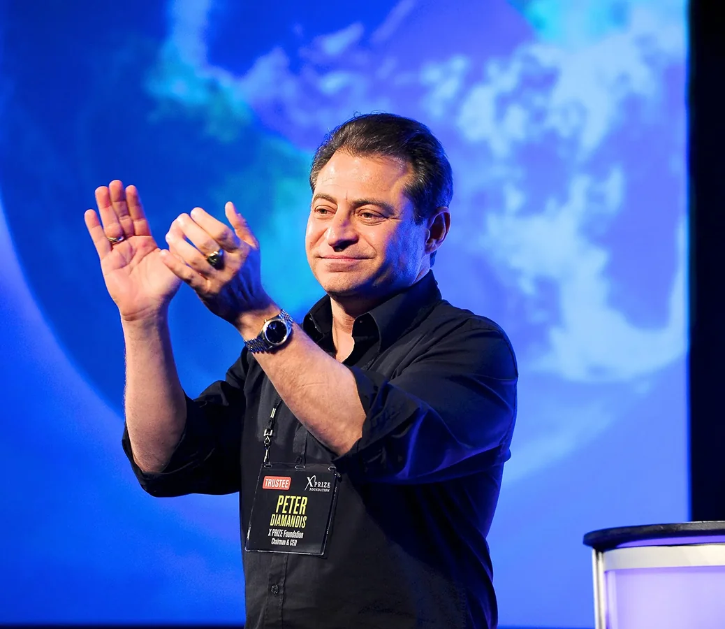 Peter Diamandis clapping on stage in front of a blue background with a large image of Earth.