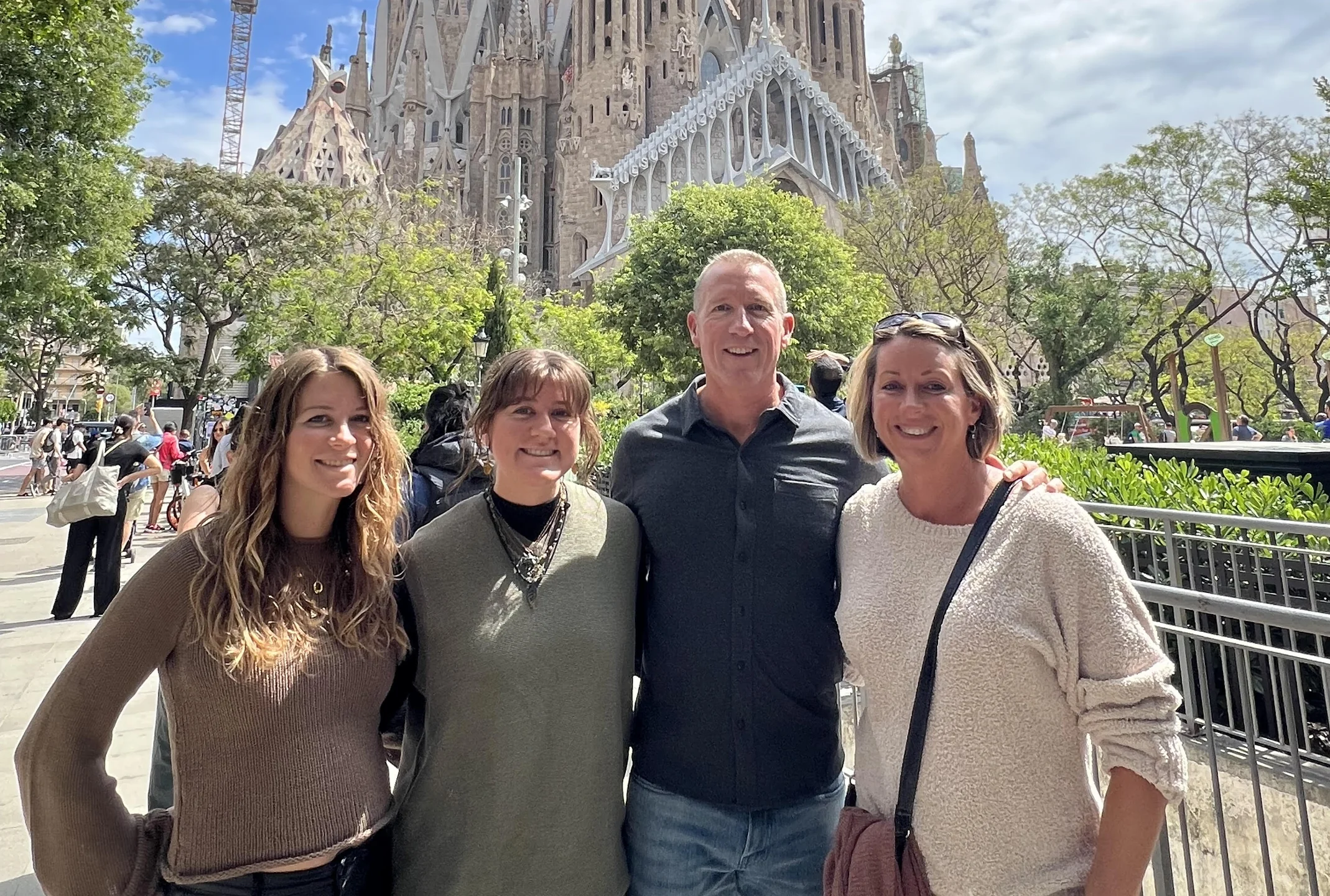 Four adults smiling and posing together outdoors with the Sagrada Família church in Barcelona in the background.