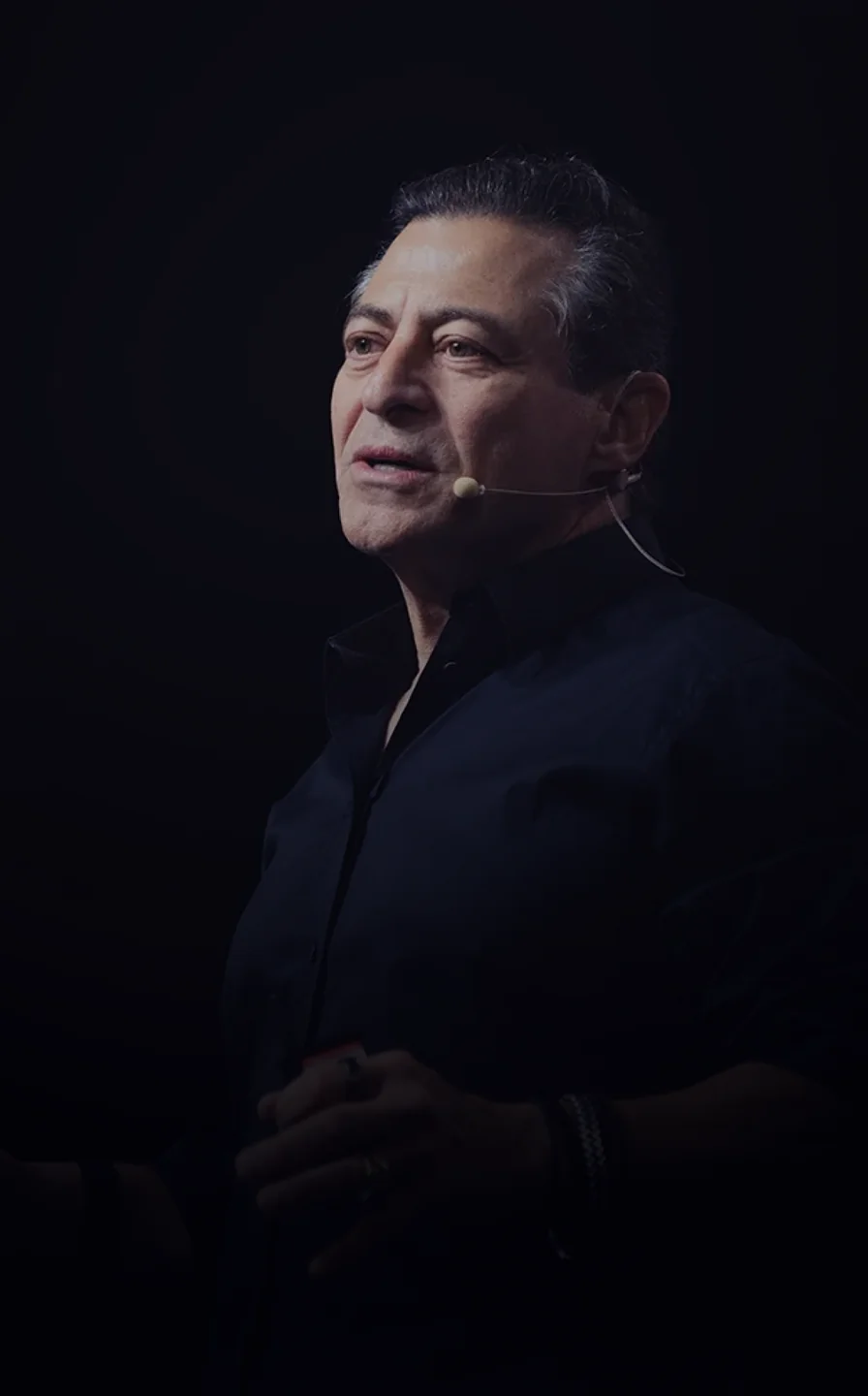 Man wearing a dark shirt and headset microphone speaking against a black background.