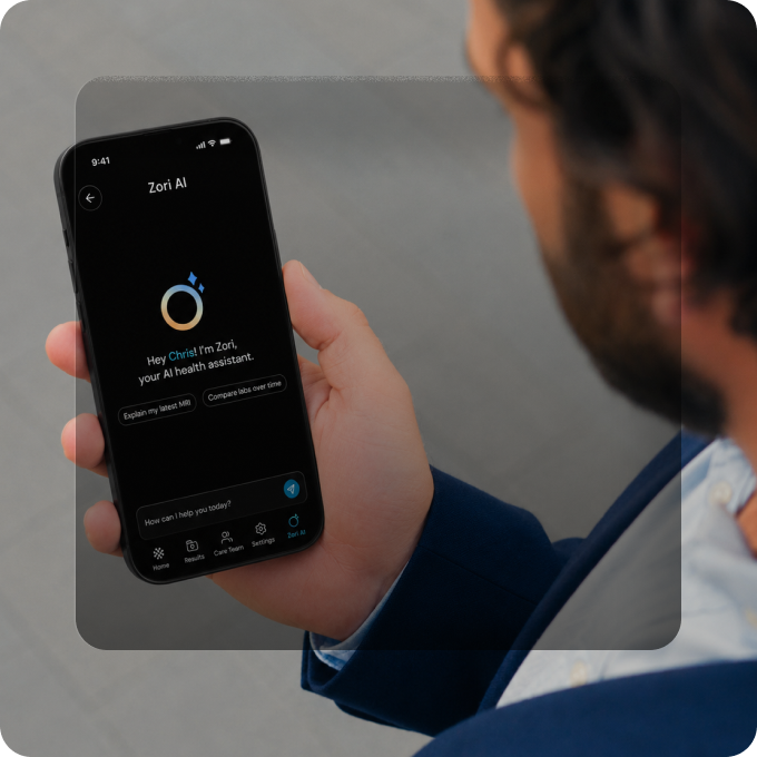 Person holding a smartphone displaying an AI health assistant app named Zori AI, greeting the user Chris and offering options to explain the latest MRI or compare lab results over time.