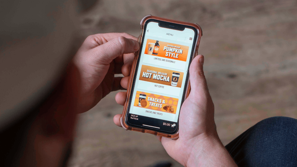 Hands hold a smartphone displaying an app menu featuring winter-themed hot beverages.