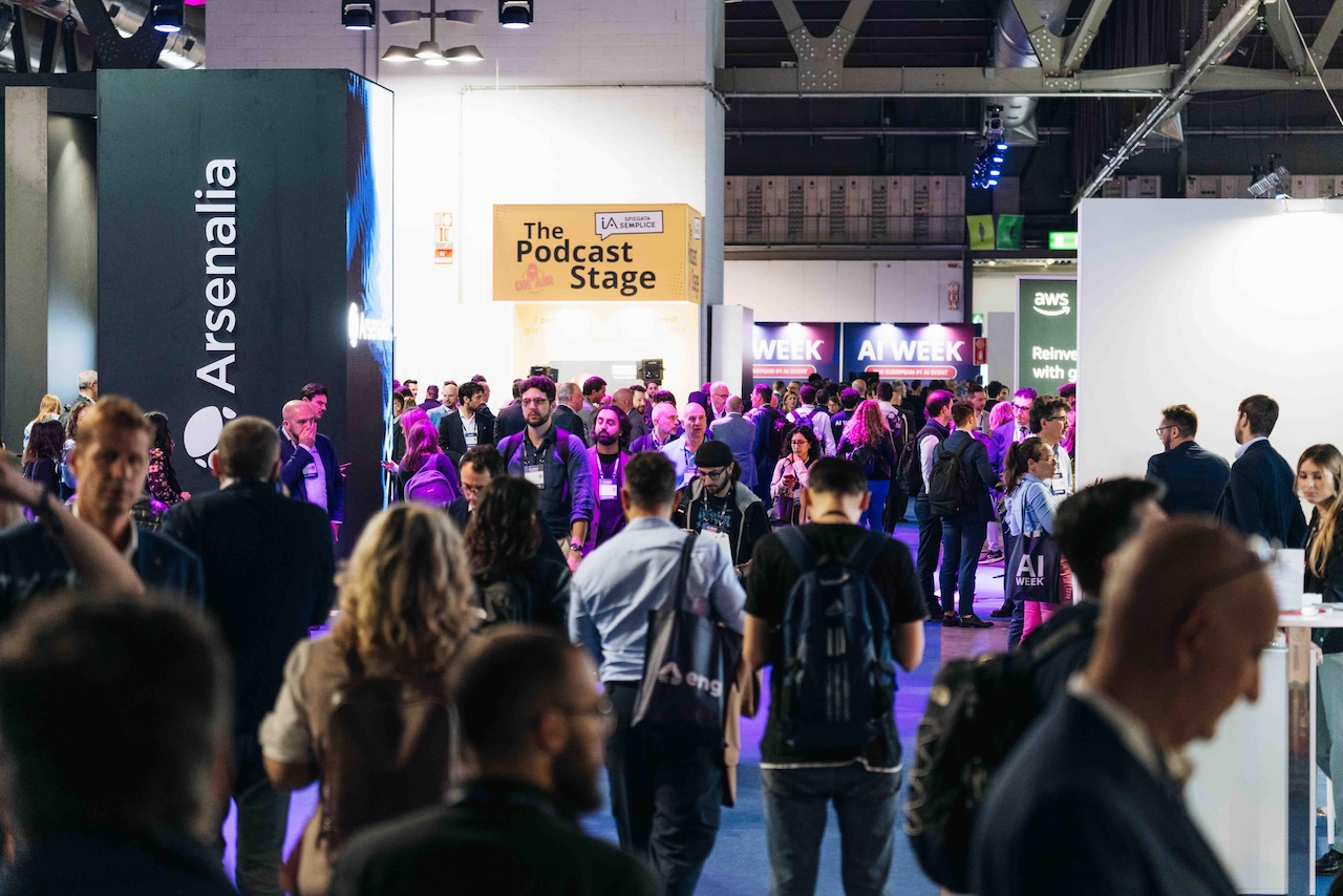 A hallway packed with event attendees walking between walls and sponsor signage.