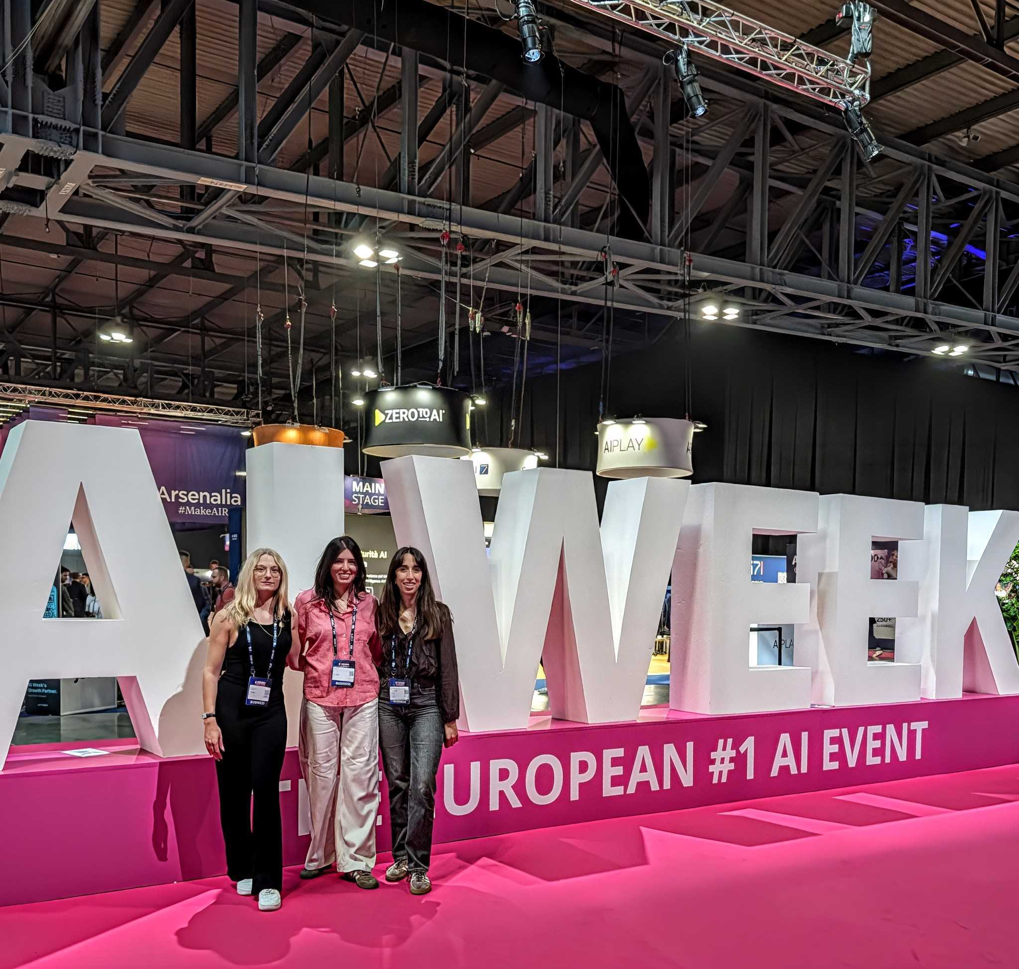 Three young women attendees wearing labels pose next to an event sign. 