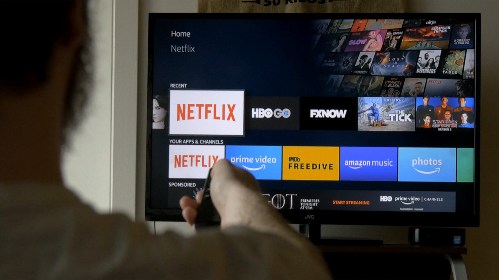 A man holds a remote towards a smart T.V. displaying streaming apps. 