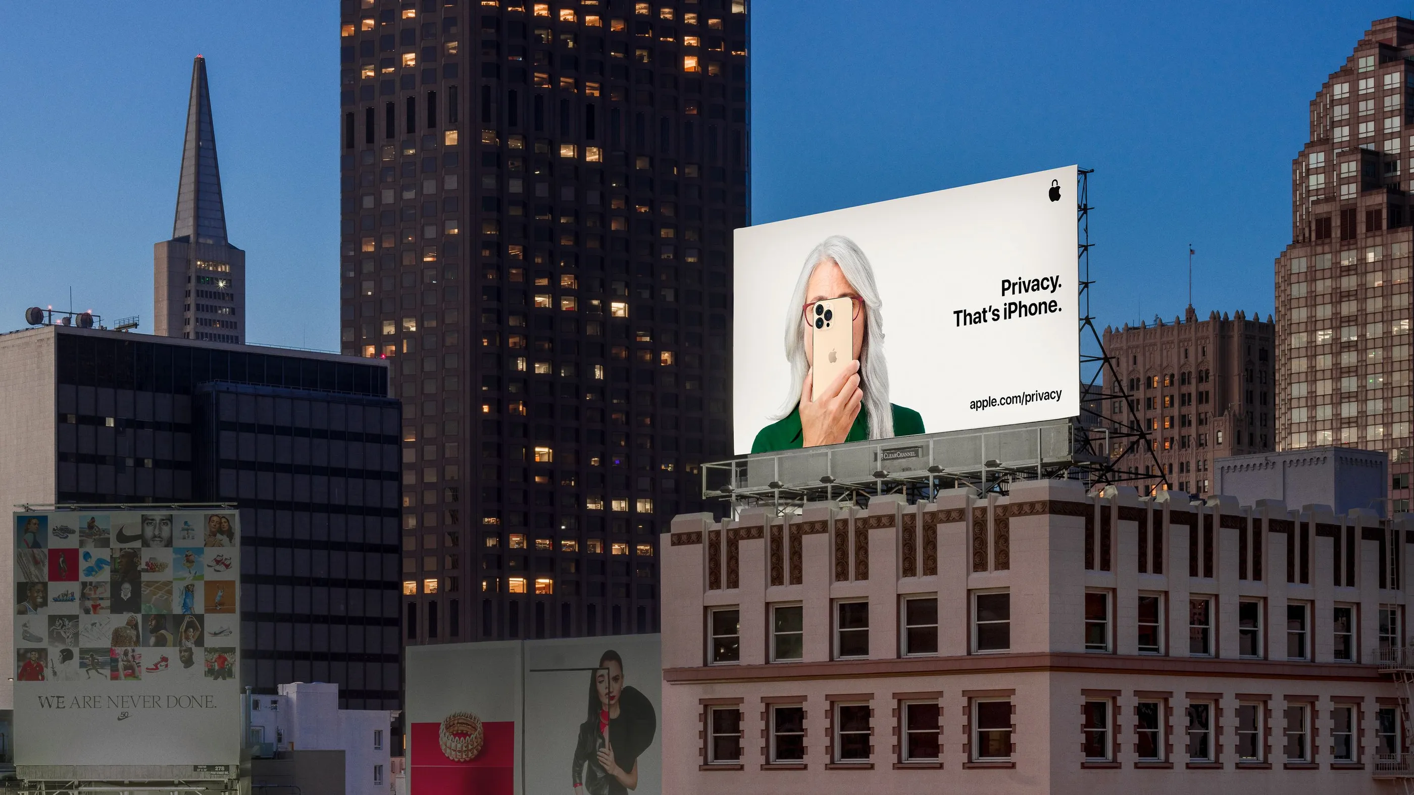 An iPhone billboard sits atop a beige building standing next to skyscrapers in a city.