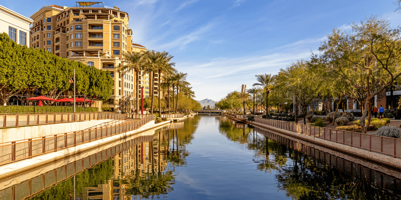 A serene canal flanked by palm trees and modern buildings under a clear blue sky.