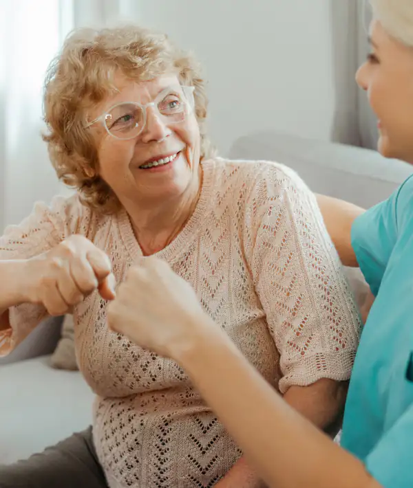 Home Care Resident sitting in a armchair with a home care helper, giving her a fist bump and they are both smiling at each other.