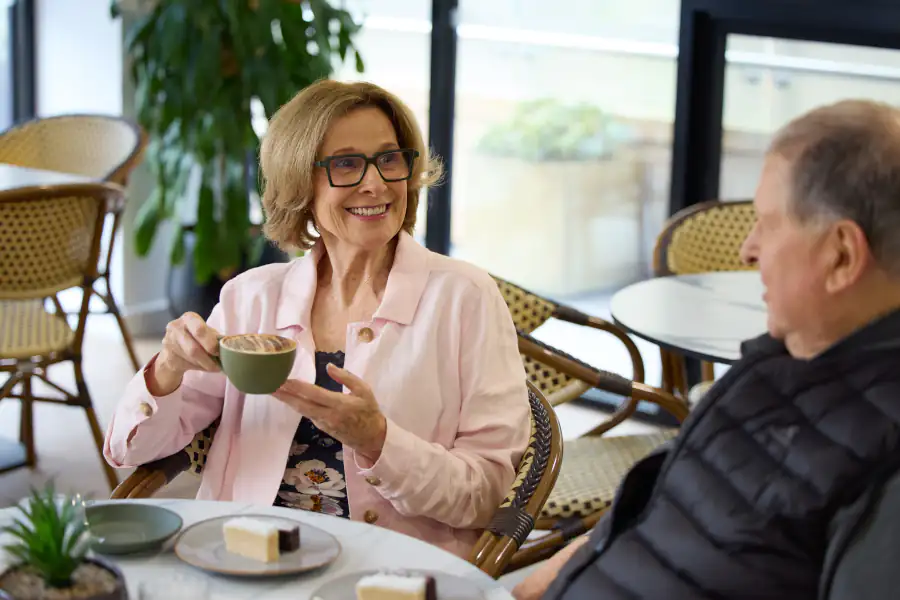 Aged care residents sitting in the Mayflower Reservoir cafe drinking coffee, eating slice and chatting.