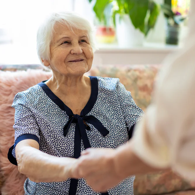 Older woman in dementia care being helped up from a chair.