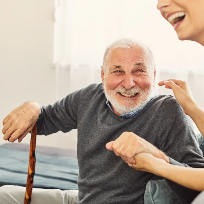 An older man man in dementia care laughing with a care worker.