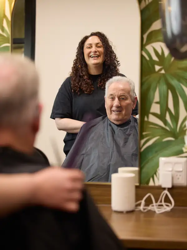 An older man at the Salon laughing with the hairdresser.