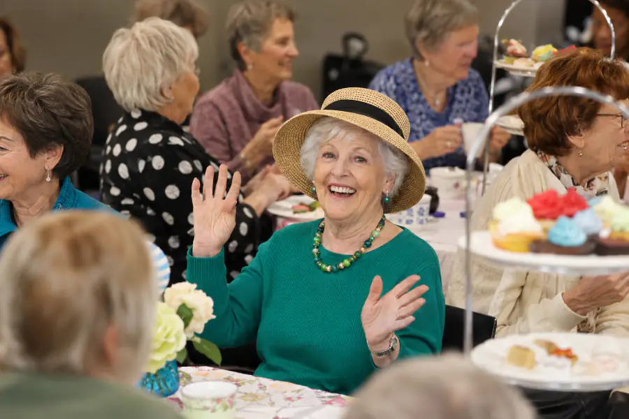 An older woman sitting at a table with cupcakes on a tiered platter, enjoying a tea party at Mayflower aged care.