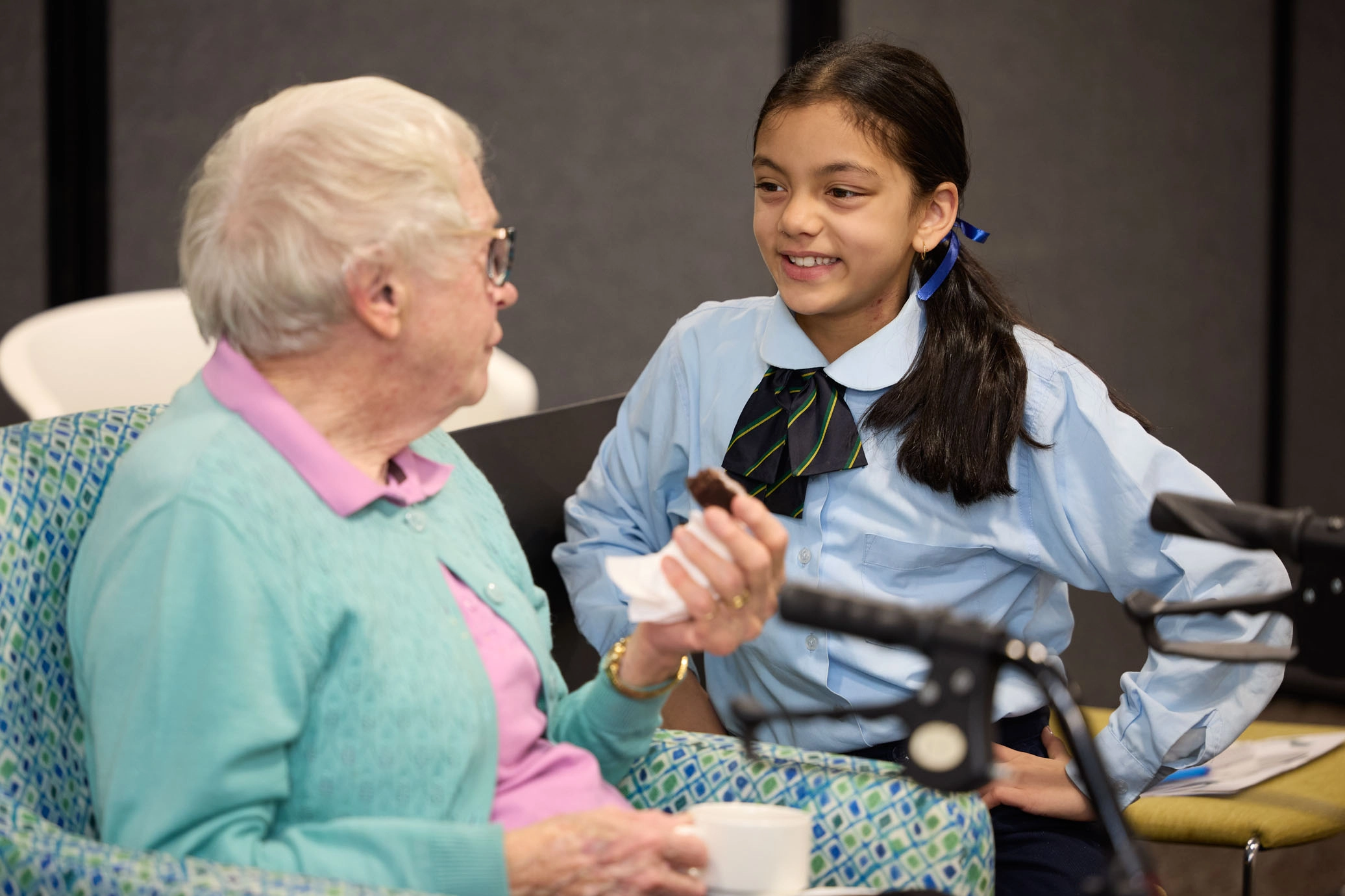 a resident enjoys a hedgehog chocolate slice while chatting with a young school child