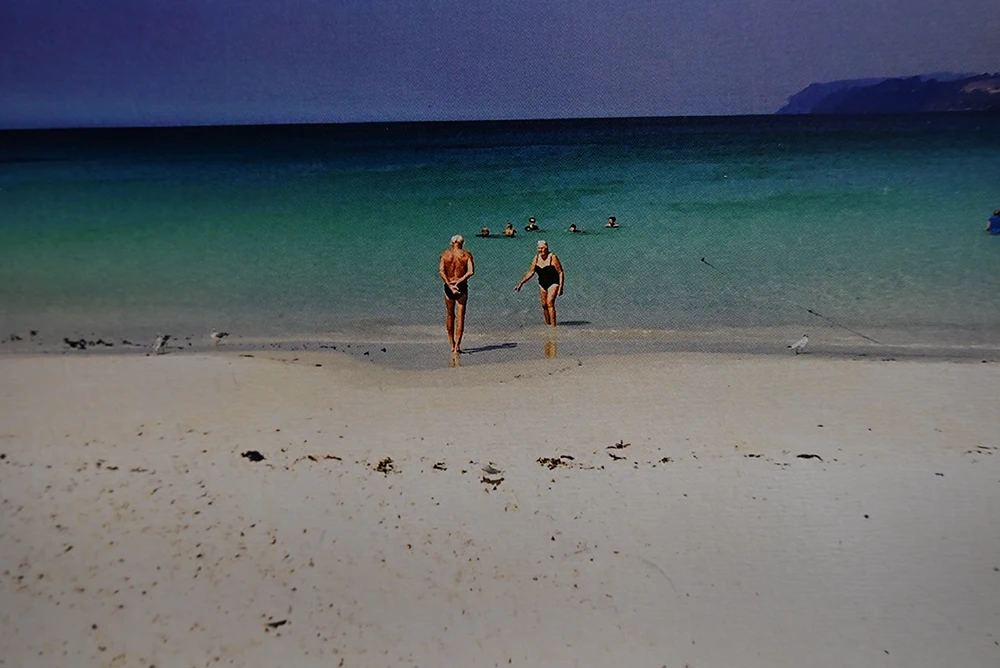 A retired couple frolicking in the water on a picturesque beach. The water is green and blue and very clear.