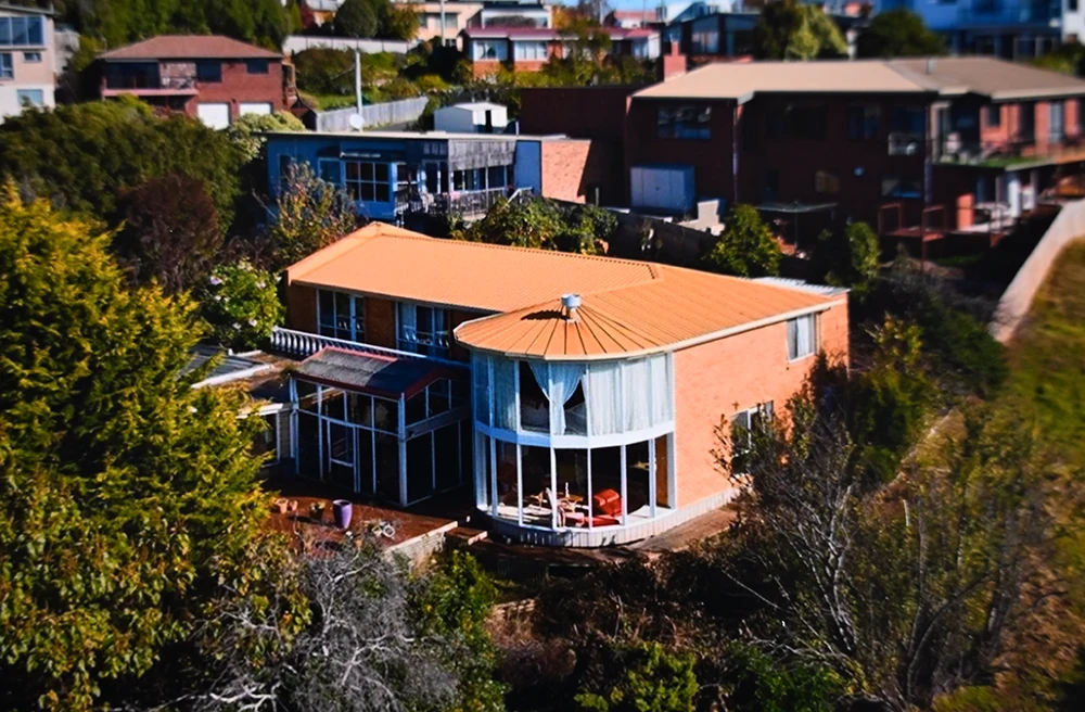 A large 2 story house on the edge of a hill, surrounded by trees.