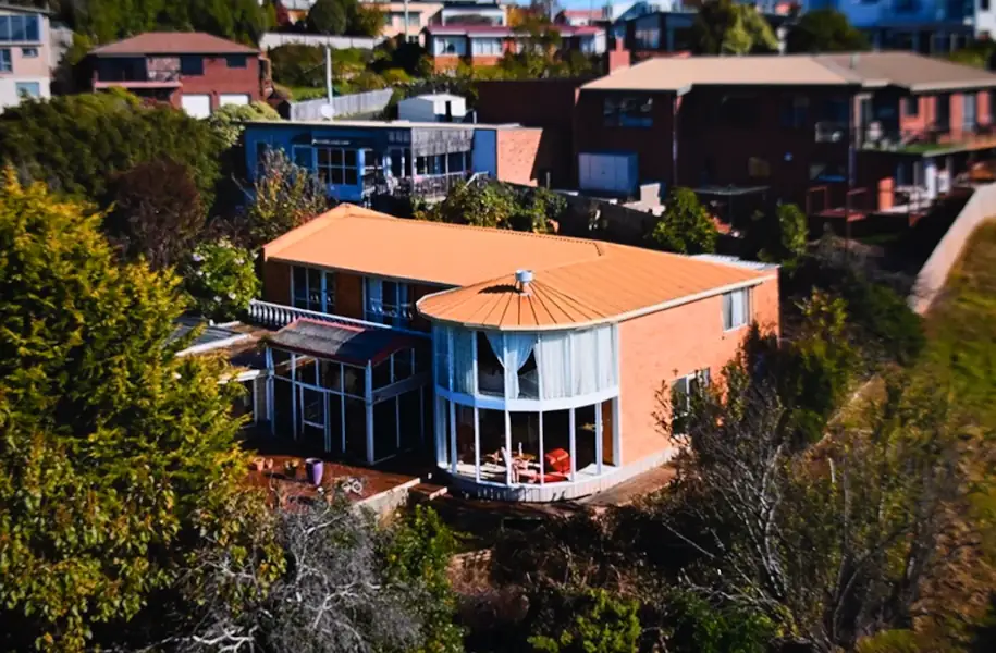 A large 2 story house on the edge of a hill, surrounded by trees.