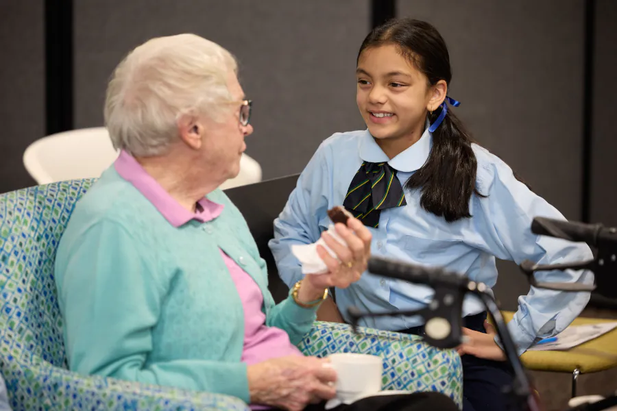 a resident enjoys a hedgehog chocolate slice while chatting with a young school child