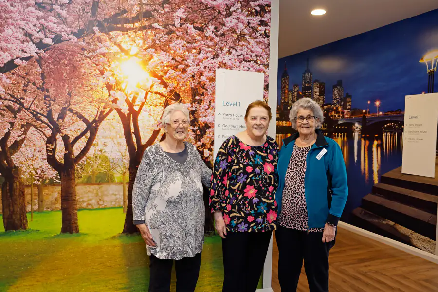 3 Women stand in front of murals depicting outdoor scenes