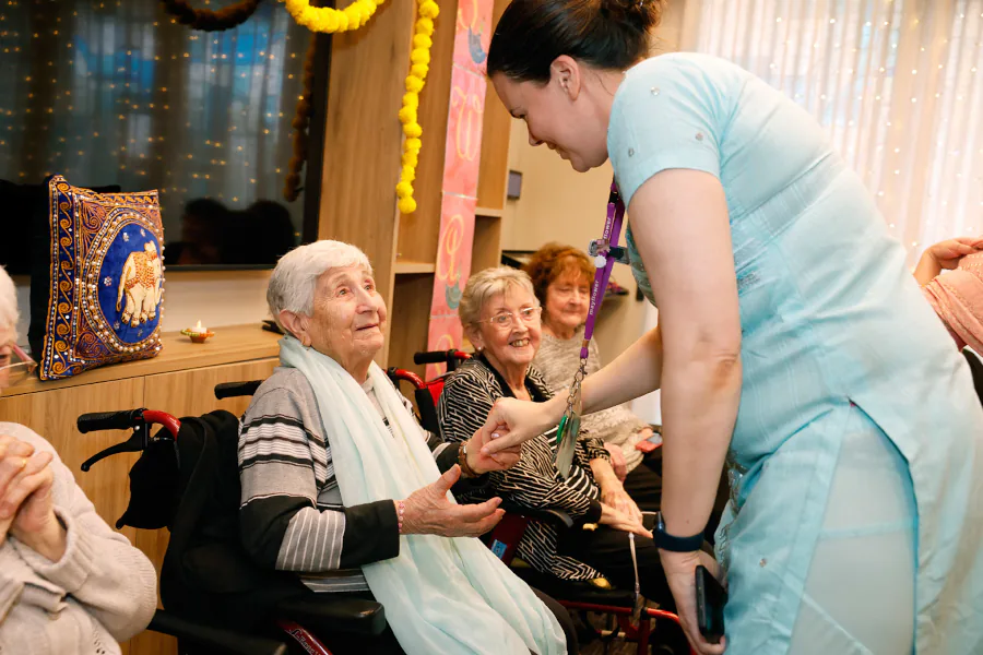 a nurse, wearing a sari, greets a resident warmly by holding her hand