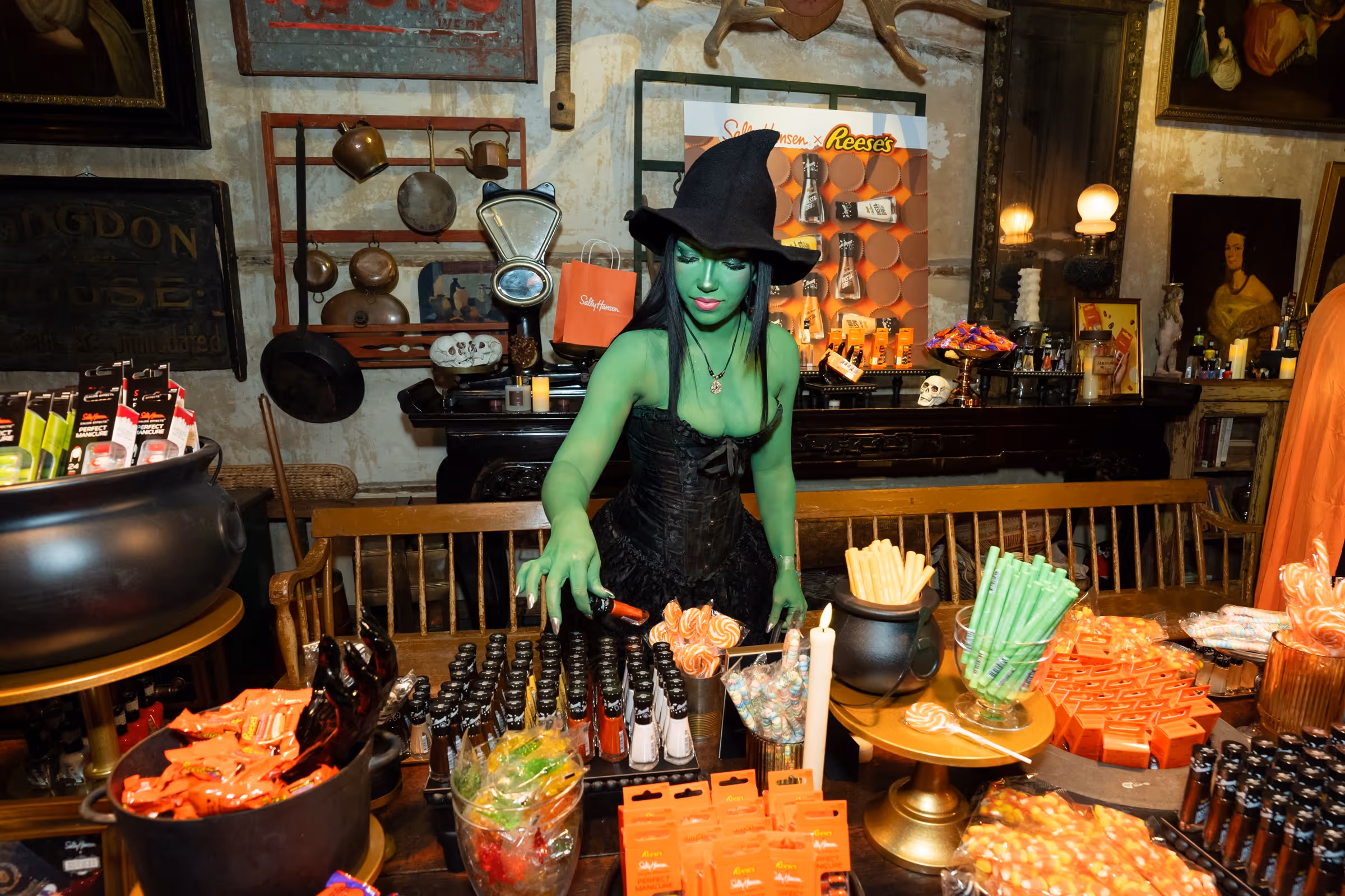 Girl in a witch costume browsing Sally Hansen nail polishers at the Halloween event.