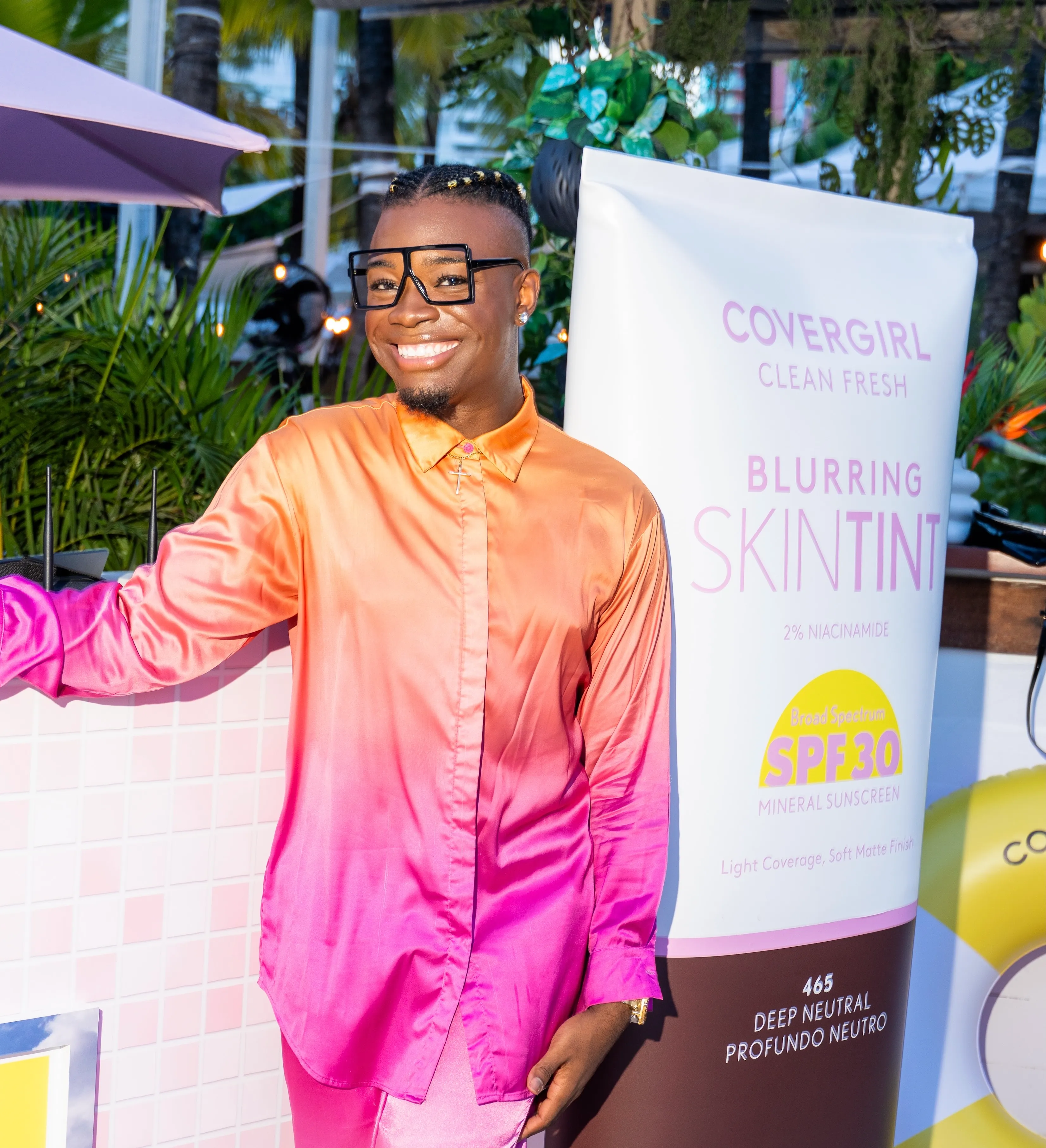 Guest posing in front of a life-size COVERGIRL Clean Fresh Blurring Skin Tint installation at Blur Beach Club, surrounded by bright pink-and-yellow decor.