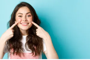 A girl smiling with one finger on her cheek 