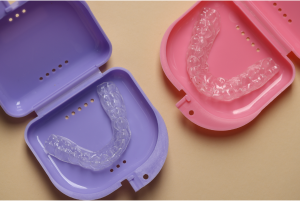 Two colourful, clear aligner cases with clear aligners in them