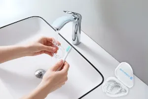 A person cleaning clear aligners with water and brush