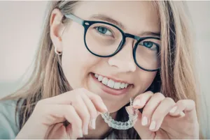 A girl smiling and holding clear aligners