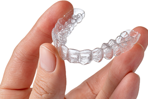 Clear plastic dental aligner held by a human hand
