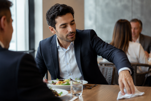  A man removing and putting his aligners in a napkin while eating mid-meeting. 